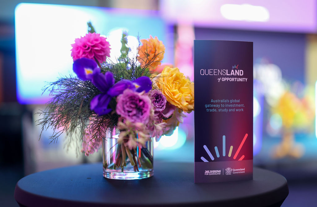 A QueensLand of Opportunity display card next to a bunch of flowers. 